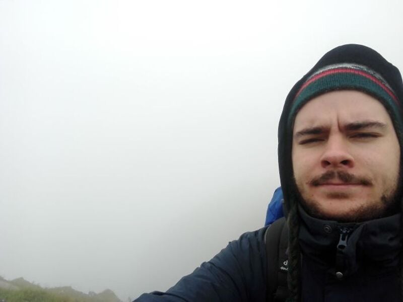 Man in winter gear on a foggy mountain hike, looking at the camera.