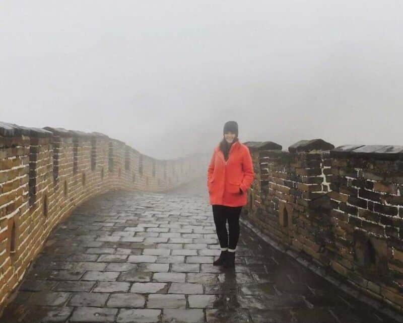 Person in red jacket walking on a foggy, wet brick pathway with brick walls on both sides.