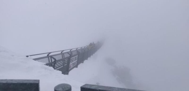 Snow-covered bridge disappearing into fog, part of a mountain scene.