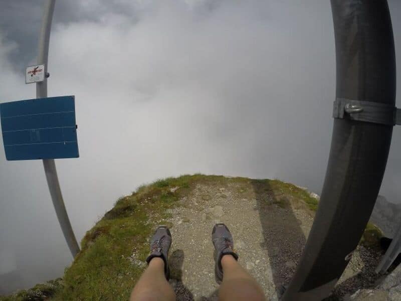 View from a mountain ledge with shoes and safety barriers, clouds below.
