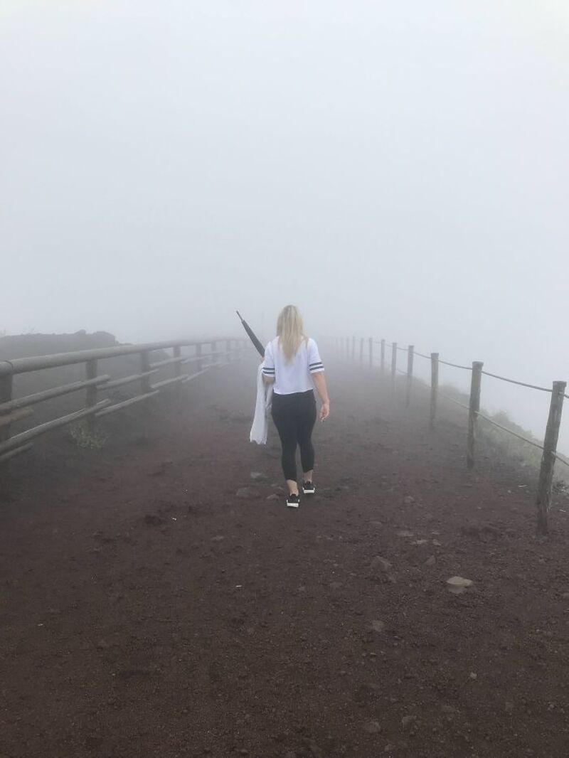 Woman walking on a foggy dirt path with a railing on each side.