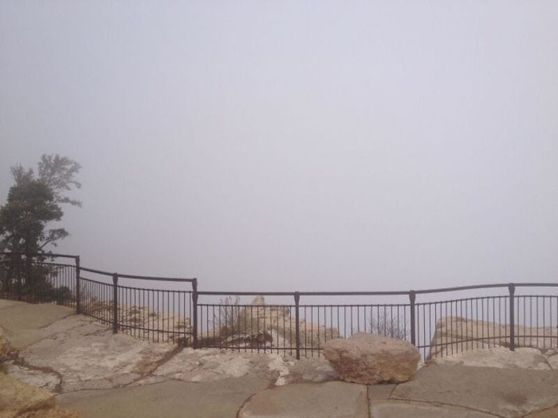 View of a foggy landscape with a metal railing and rocks in the foreground.