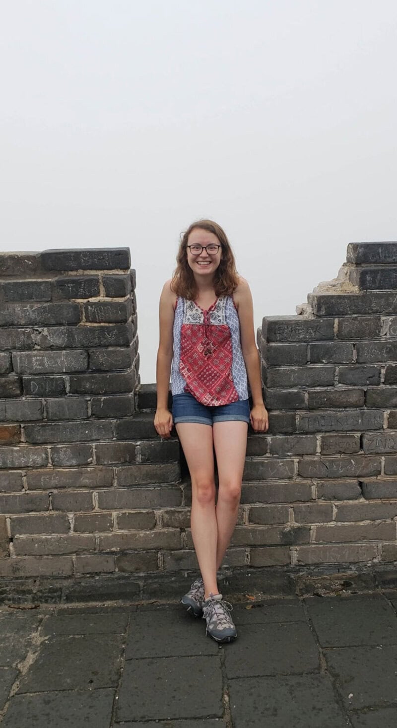 Young woman standing on a brick wall with a cloudy sky background.