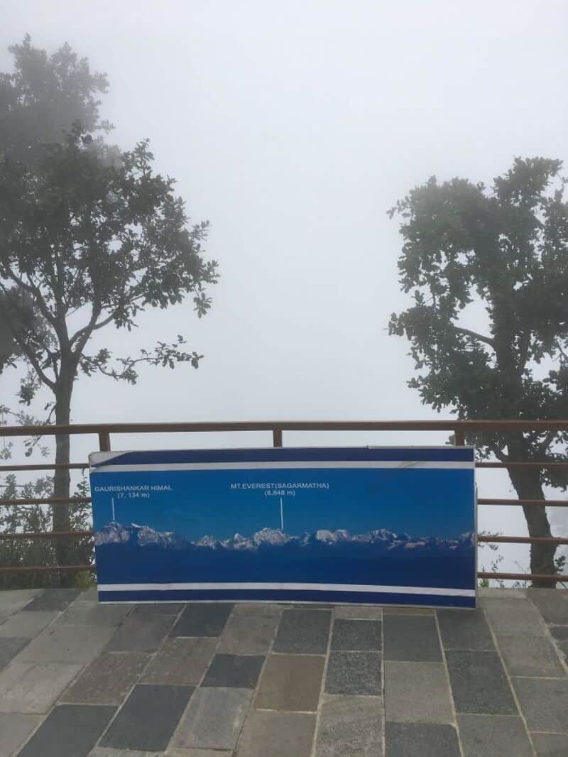 View of snow-capped mountains through fog with a blue informational sign in the foreground.