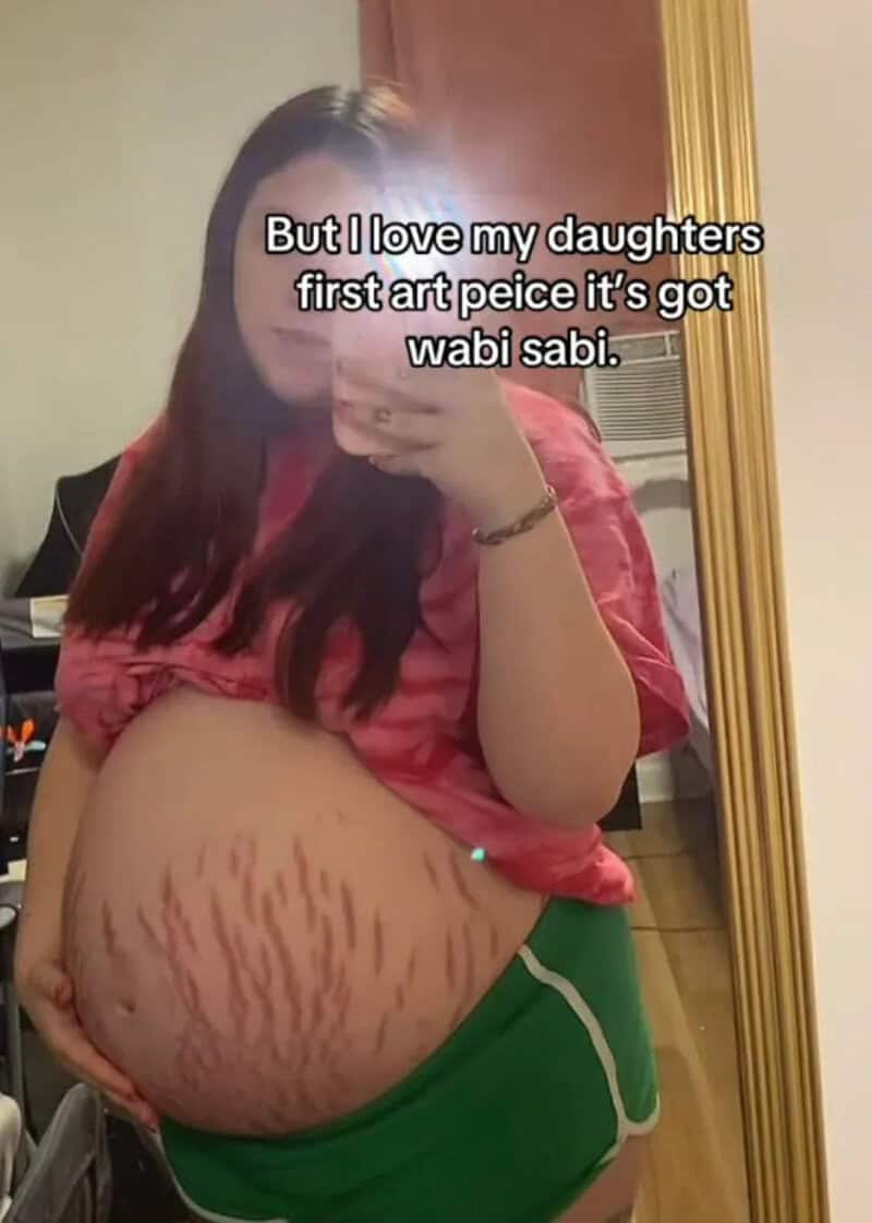Woman with stretch marks on her pregnant belly, taking a mirror selfie.
