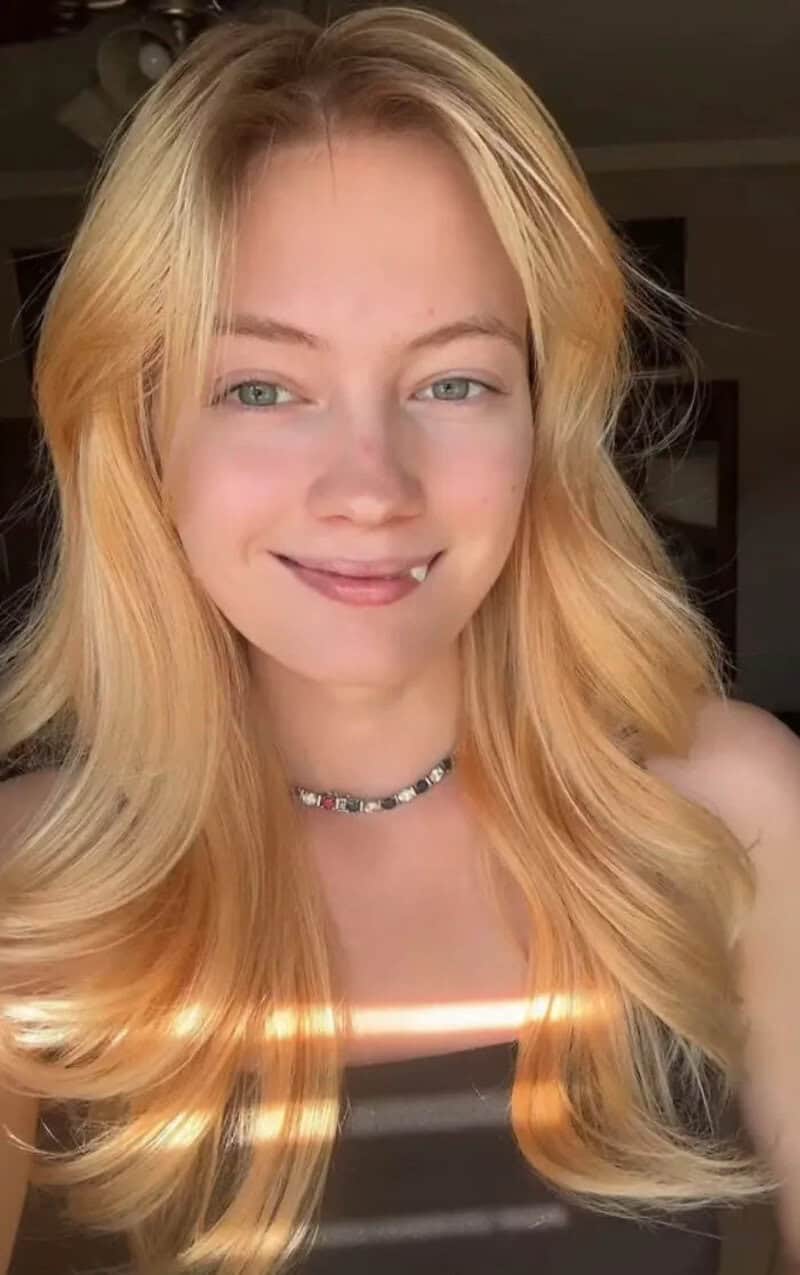 Young woman with long blonde hair smiling, sunlight on her face.