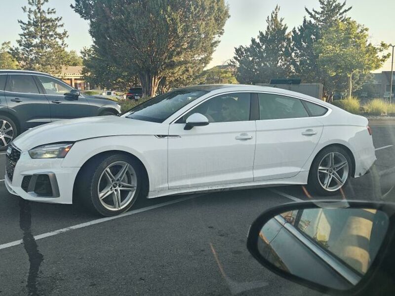 White sedan parked in a lot with trees and other cars around.