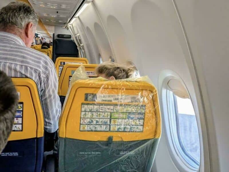 Passenger on airplane with yellow headrest and window view.