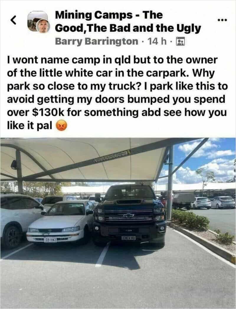 Photo of a black truck parked between two white cars in a parking lot.