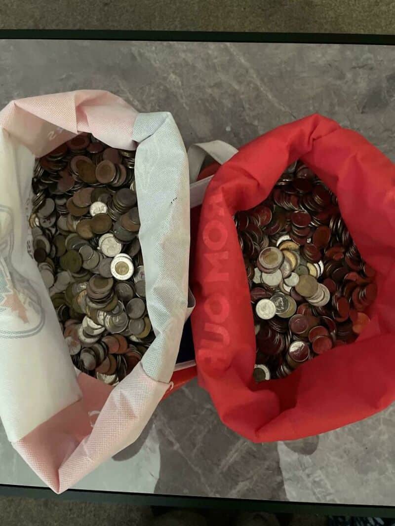 Two bags filled with coins, one white and one red, on a gray surface.