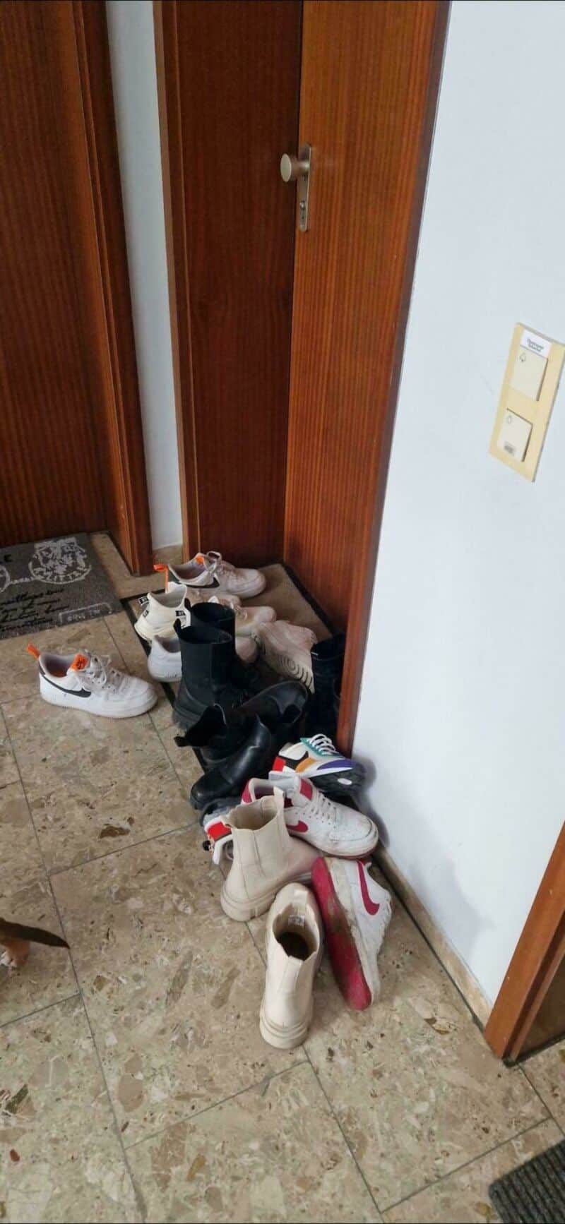 Clothes and shoes scattered near a wooden door and light switch.