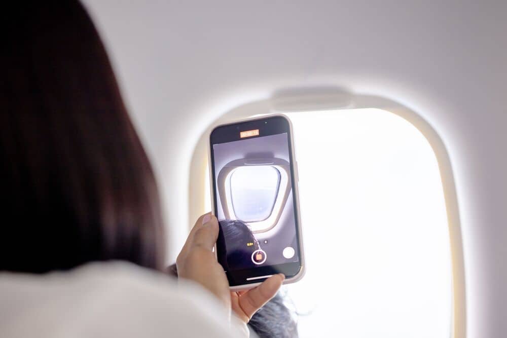 Person taking a photo of the airplane window with a smartphone.