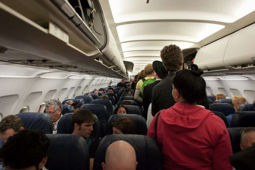 Passengers standing in the aisle of an airplane cabin during boarding.