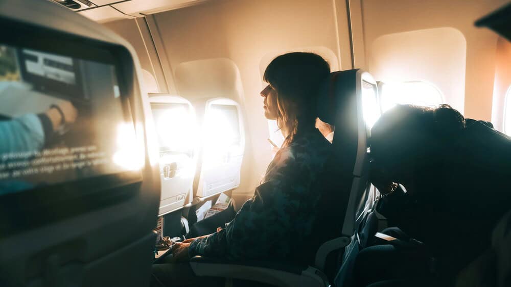 Passenger sitting by window on airplane, looking at in-flight entertainment.