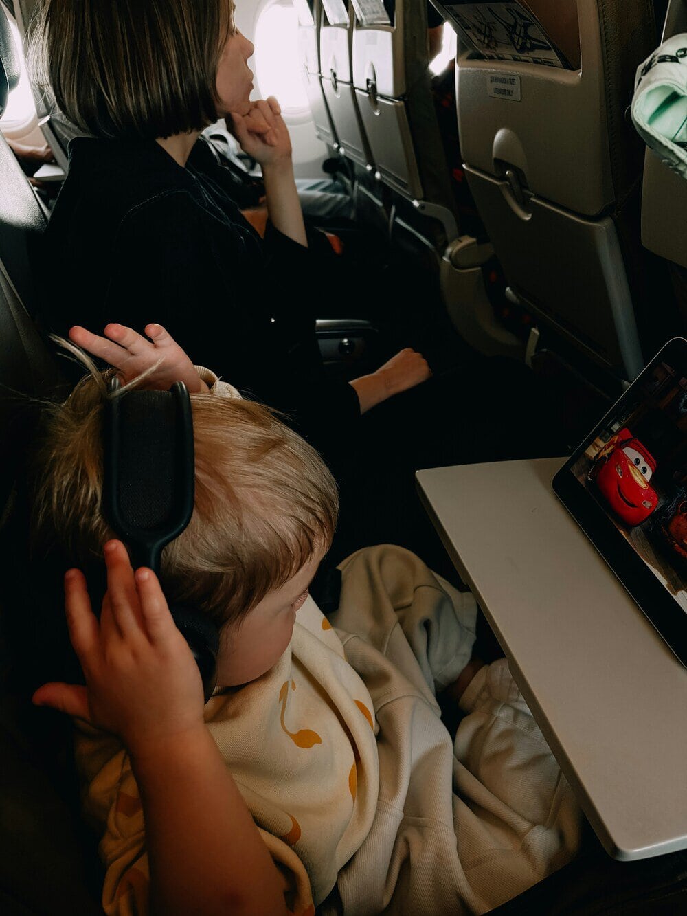Children watching a movie on airplane seat screens, one with headphones.