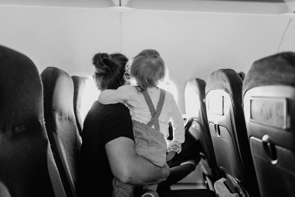 Person with a child on their lap on an airplane seat, both looking out the window.