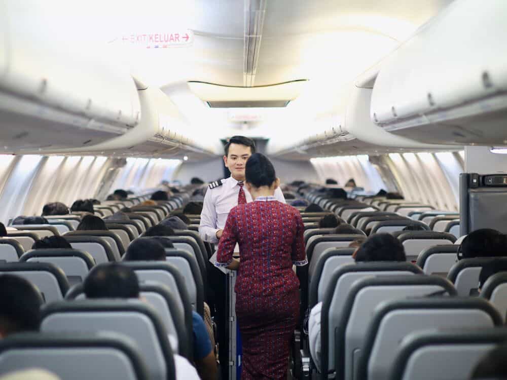 Flight attendant talking to a passenger in an airplane aisle.