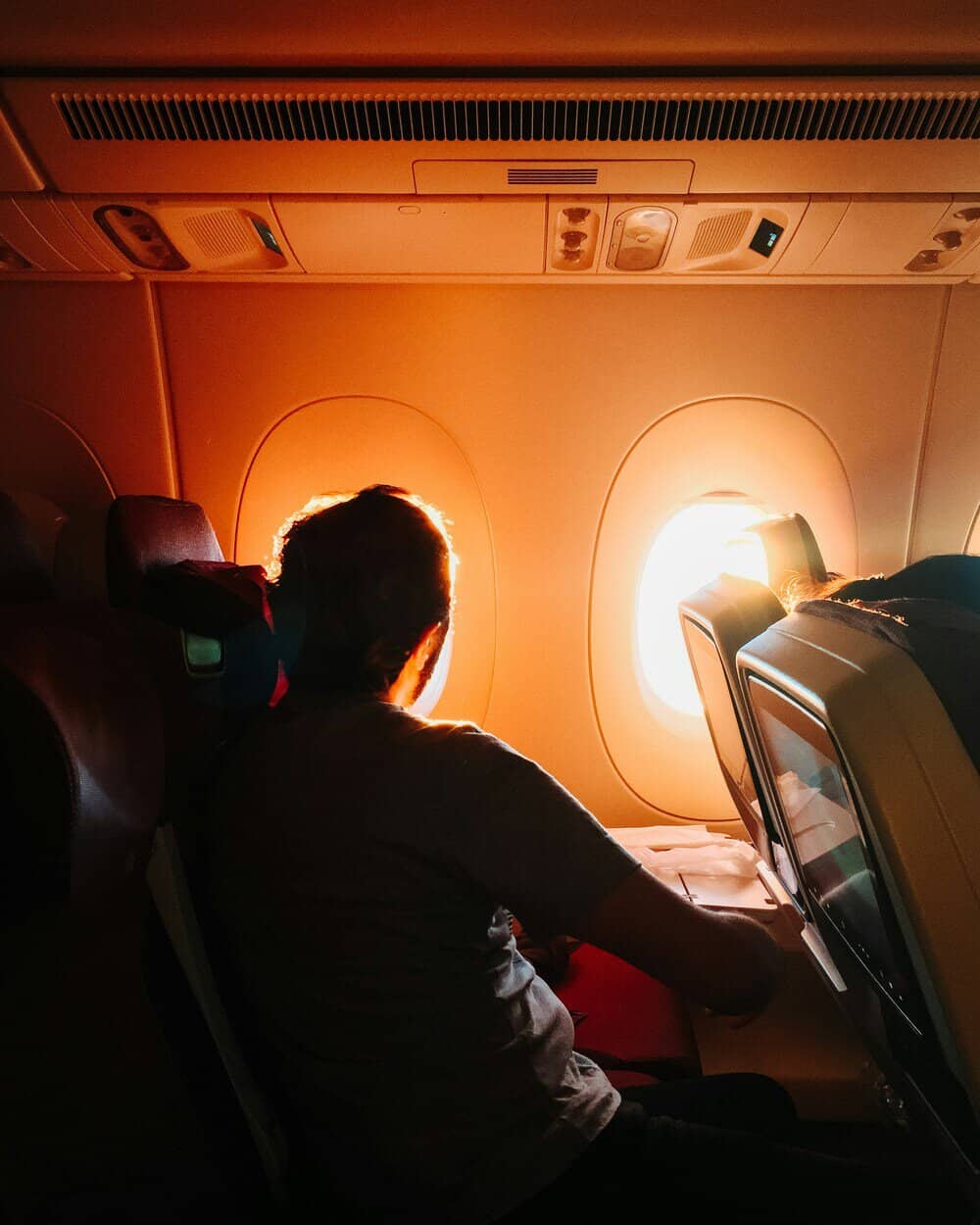 Passenger looking out airplane window during sunset or sunrise.