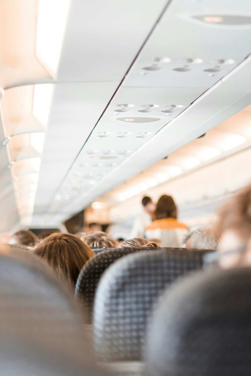 Inside view of an airplane cabin with passengers seated and overhead compartments.
