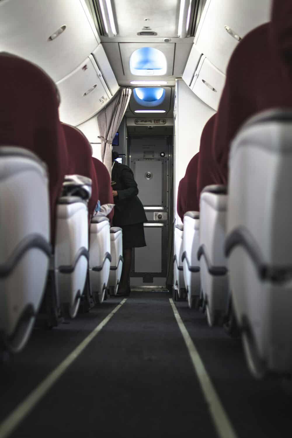 View of airplane interior with seats and a person walking down the aisle.