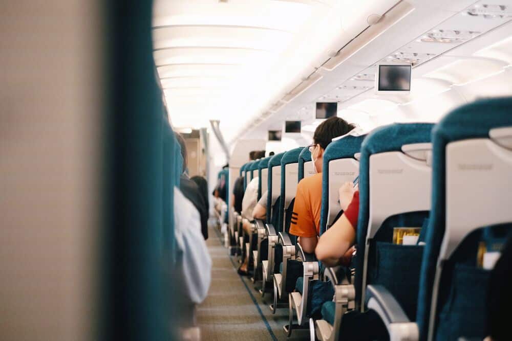 Inside an airplane cabin with passengers seated, viewed from the aisle.