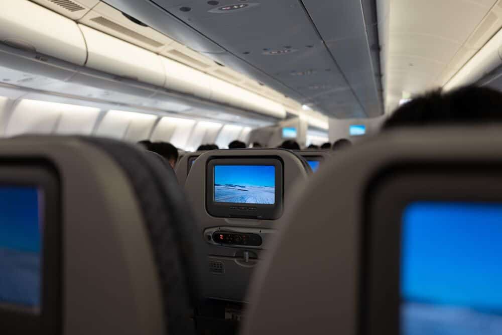 View of airplane cabin with in-flight entertainment screens on seats.