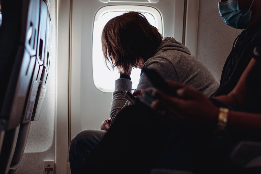 Person sitting on airplane seat looking out the window, with another person beside them.