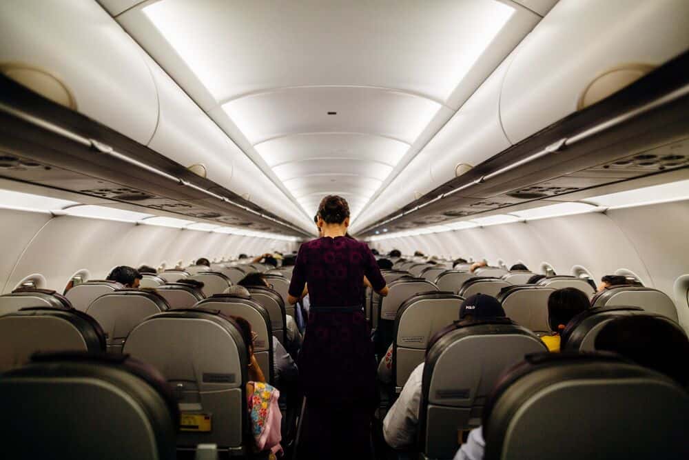 Passenger walking down the aisle of an airplane with seated passengers on both sides.