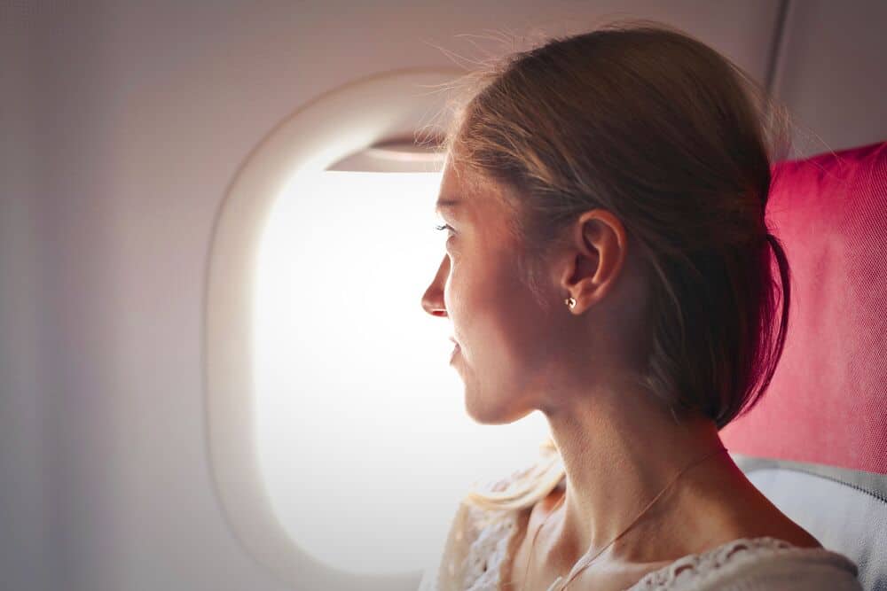 Woman looking out airplane window, profile view, with sunlight on her face.