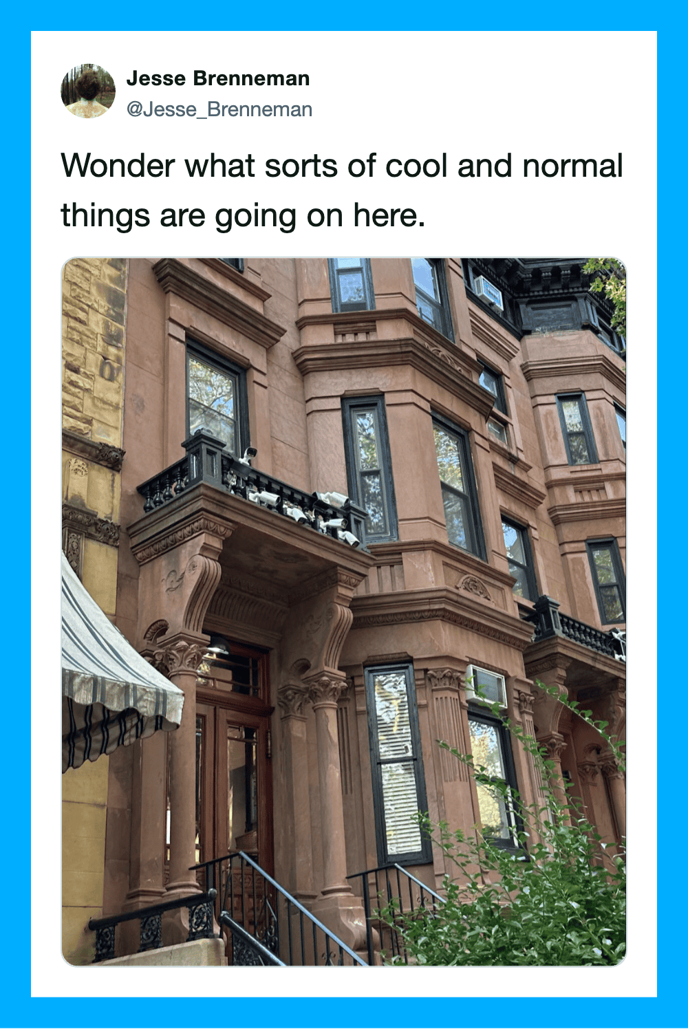 Brownstone building with bay windows and a small balcony, with a striped awning in front.