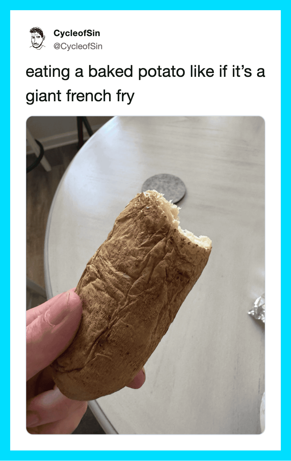 Person holding a baked potato with a bite taken out, on a table.