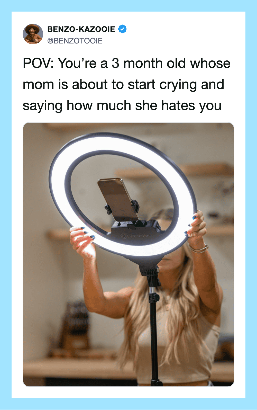 A woman holding a ring light with a phone attached, in a kitchen setting.