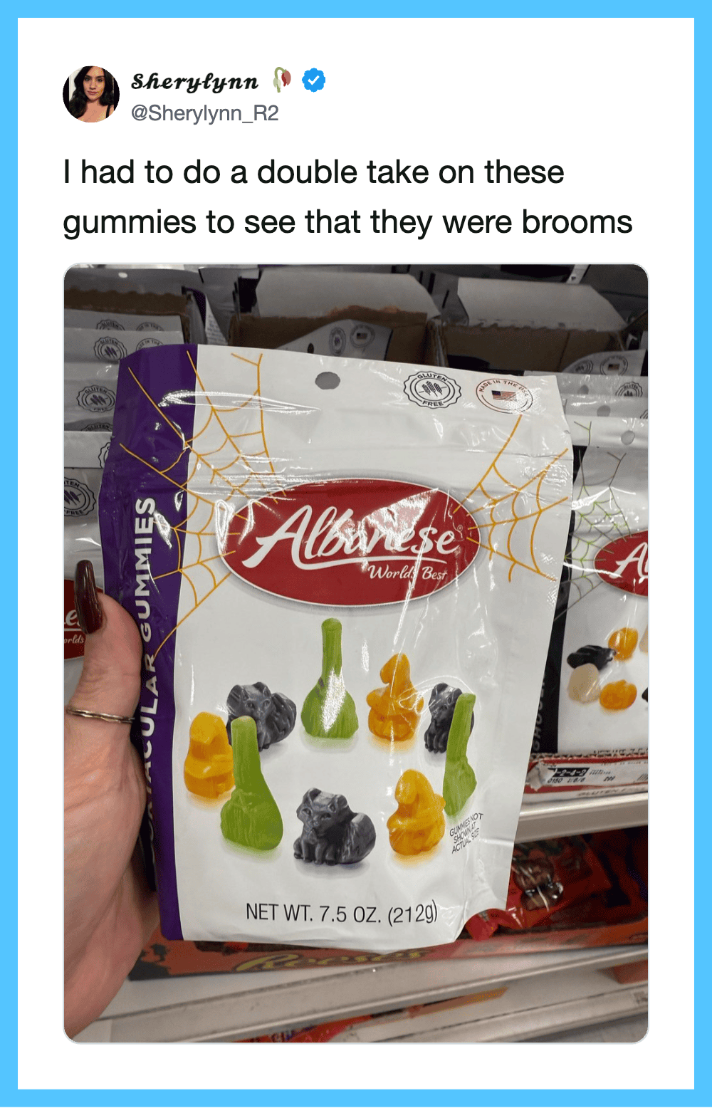 Hand holding a bag of gummy worms shaped like brooms, with other bags in the background.