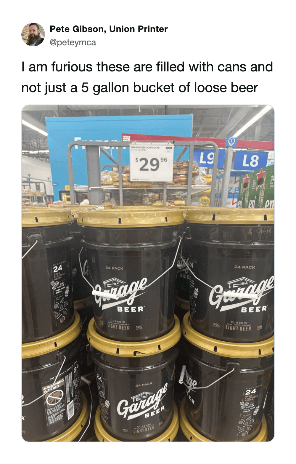 Stacked black buckets of Garage Beer with yellow lids at a store, price sign in background.