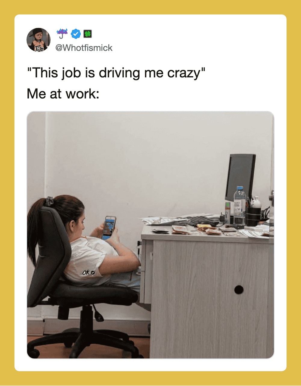 Person sitting at desk looking at phone with work items on desk.