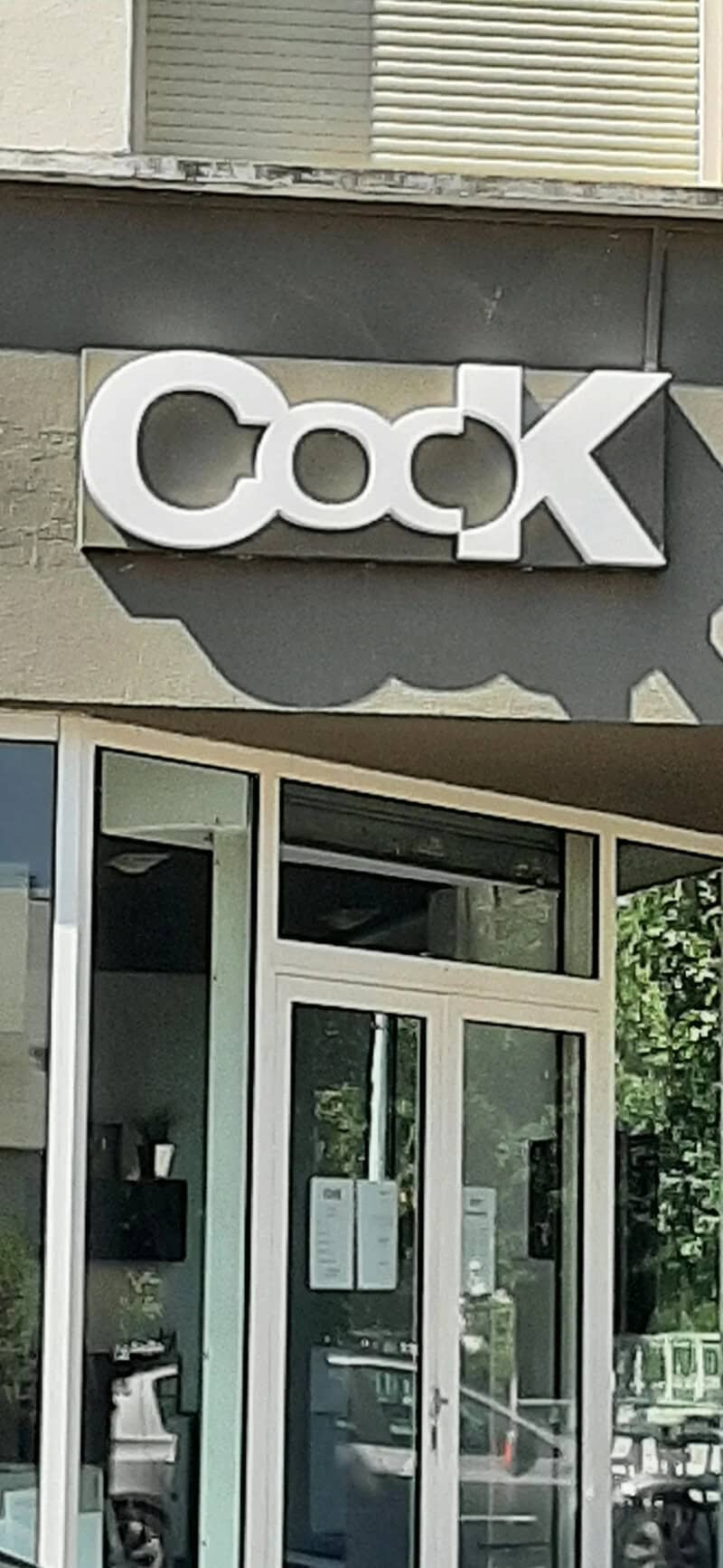 Sign with the word 'Cock' in large white letters outside a building.