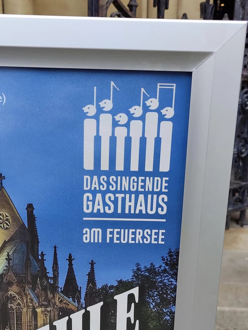 Sign with musical notes and German text 'Das singende Gasthaus am Feuersee'.