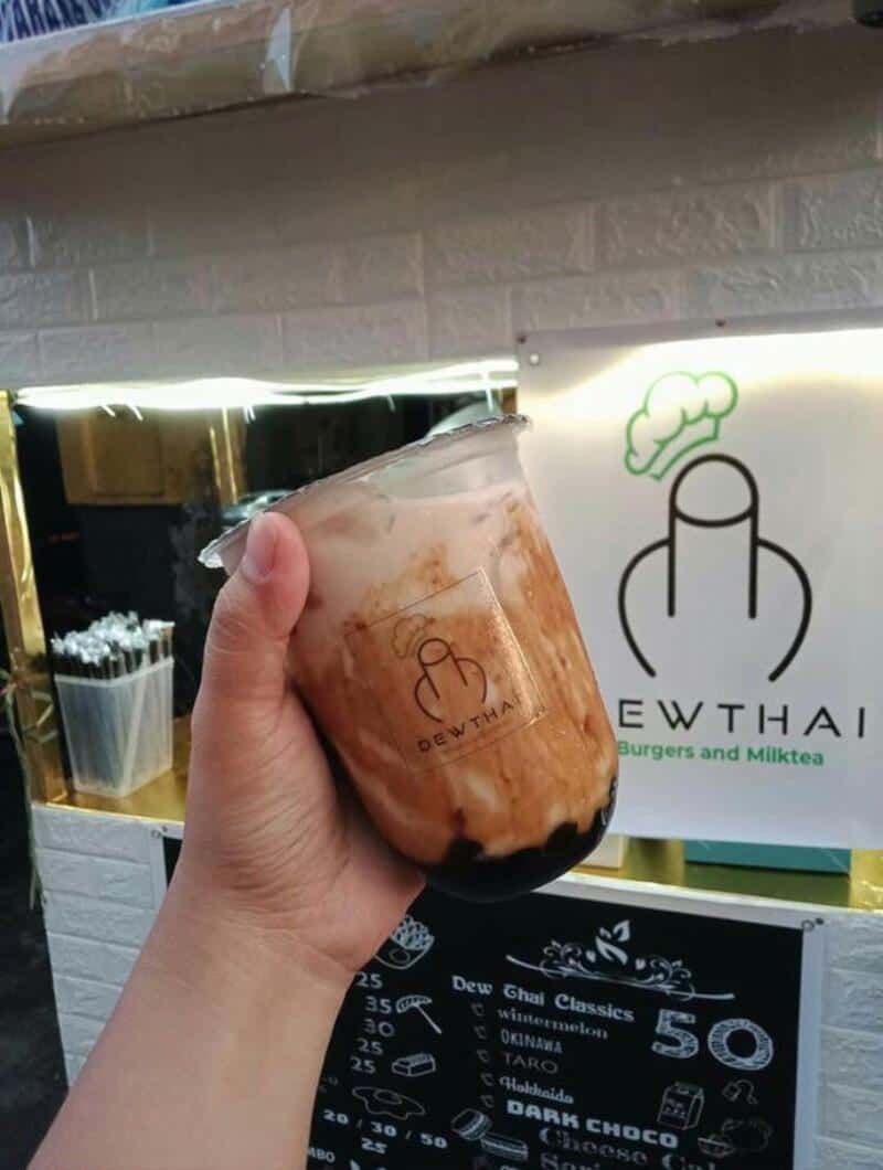 Hand holding a glass of brown and black bubble tea with a logo on it.