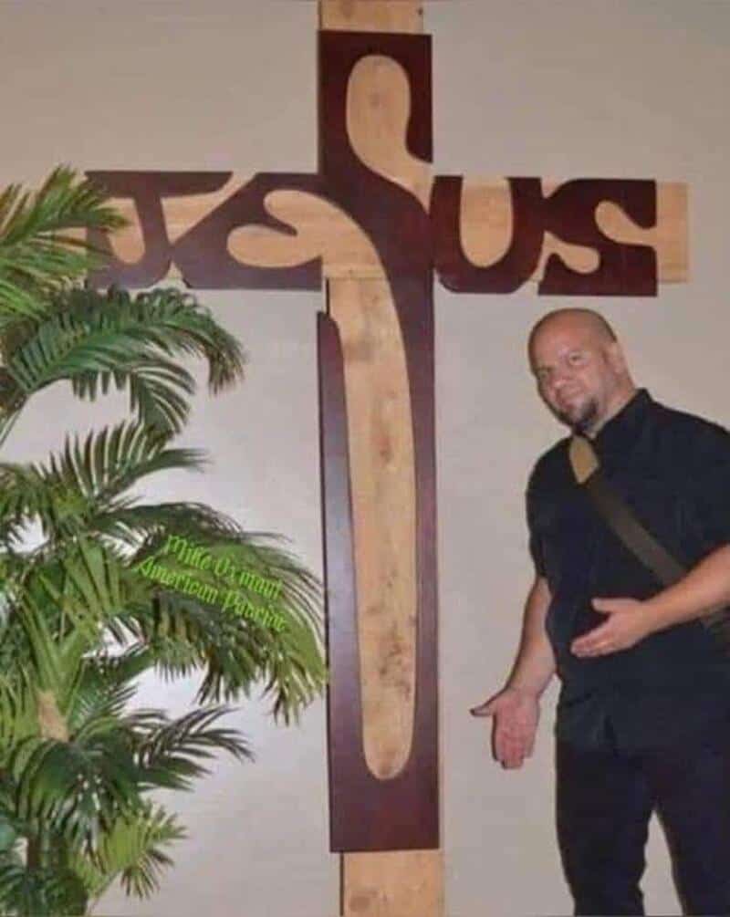 Man standing next to a cross with the word 'JESUS' on it, pointing at the bottom.