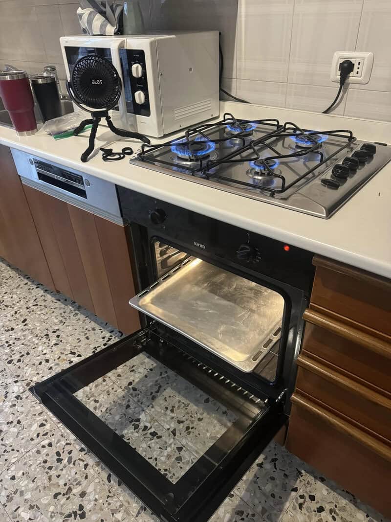 Oven with an empty baking tray and a gas stove on top in a kitchen.