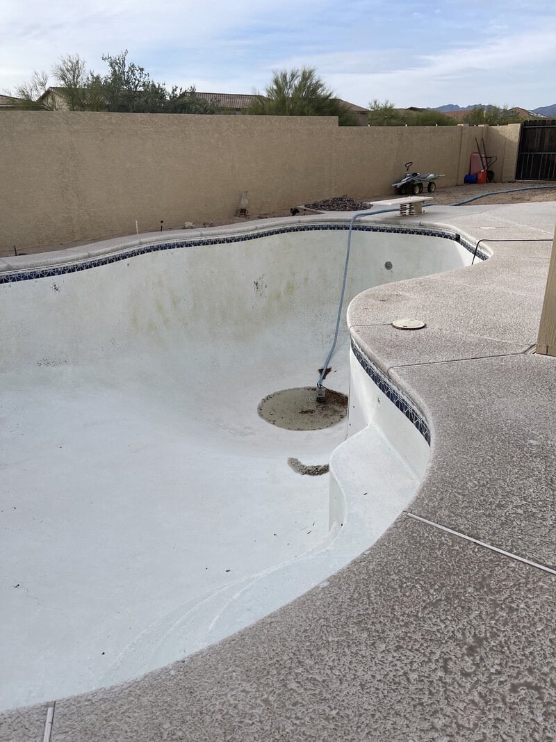 Empty swimming pool with a cleaning pole inside, no water, and a cloudy sky.