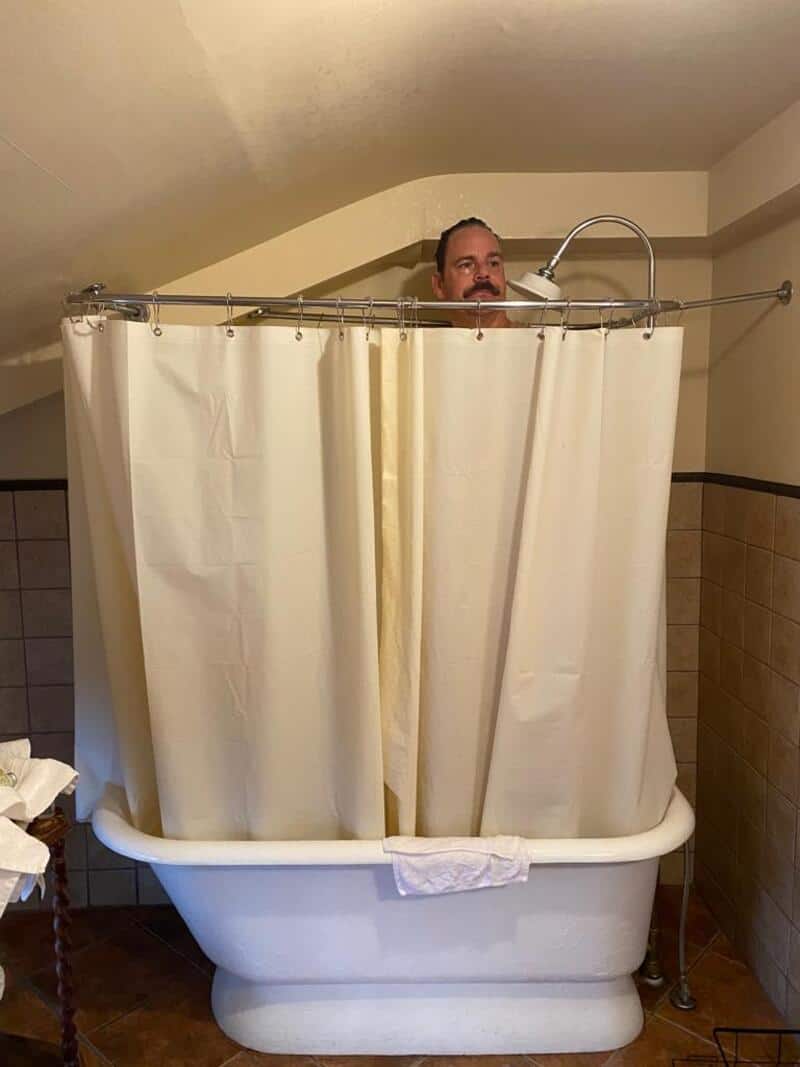 Man peeking over bathtub with shower curtain in a bathroom.