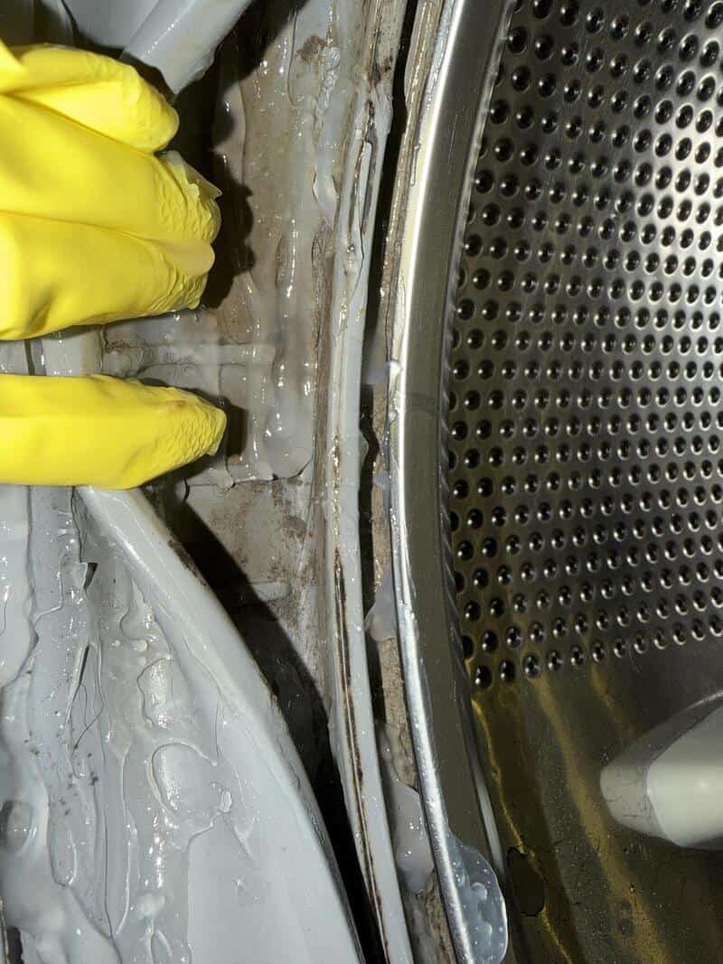 Close-up of a washing machine door with a broken seal and water leakage.