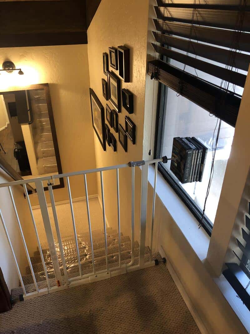 View of a staircase with a white safety gate, wall art, and a window with blinds.