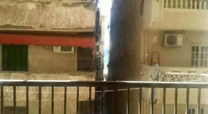 View of a narrow alley between buildings with a balcony and air conditioning units.