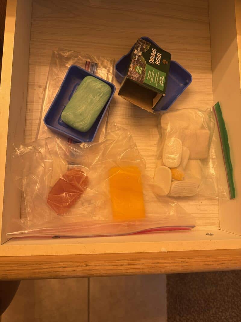 Disorganized soap and toiletries in a drawer, including soap, shampoo, and other items.