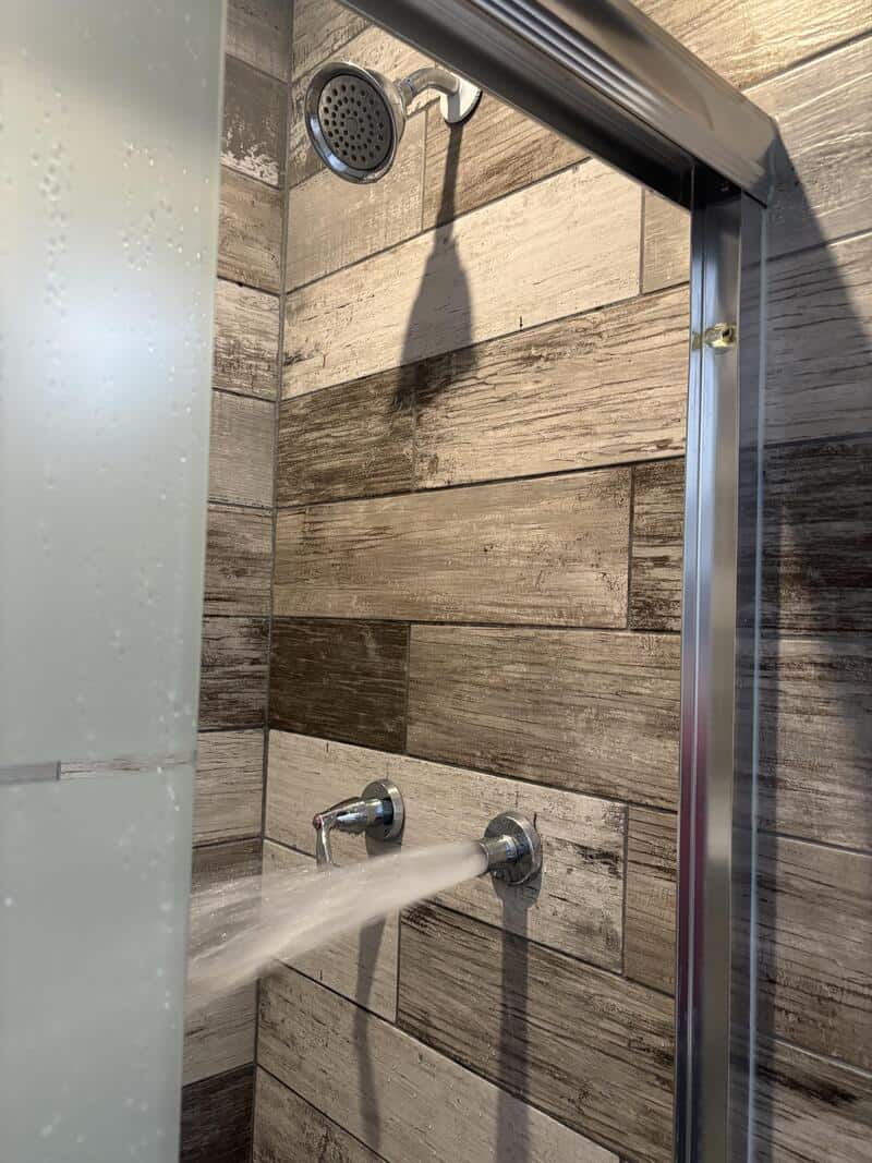 Shower with water flowing from two fixtures in a tiled bathroom.