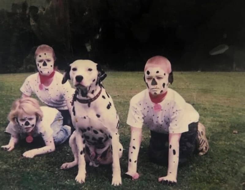 Four children and a Dalmatian dog with face paint on grass.