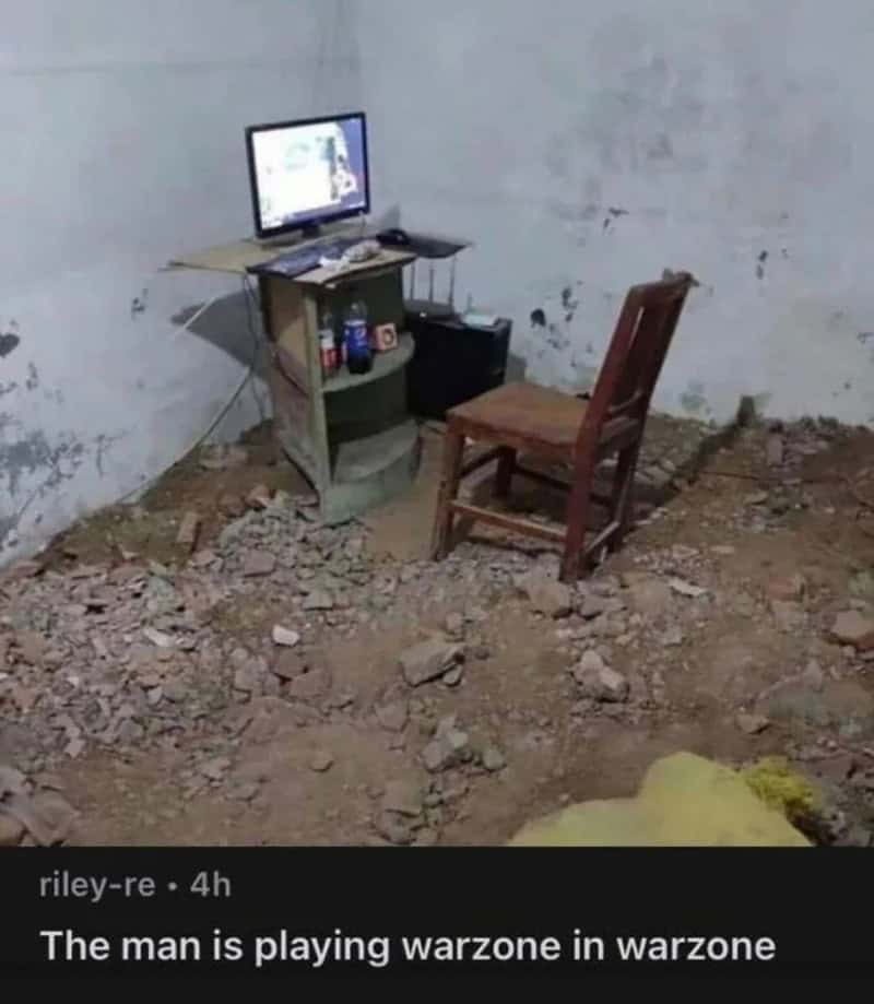A computer on a small table with a chair in a dirt-floored room, playing Warzone.