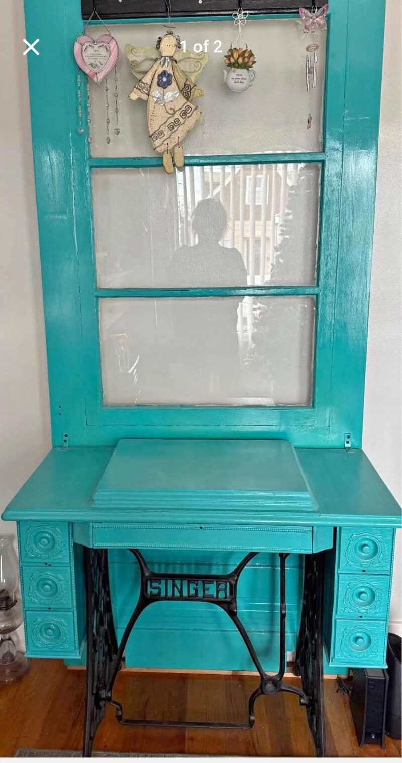 A turquoise vintage sewing machine table with a mirror and decorative items.